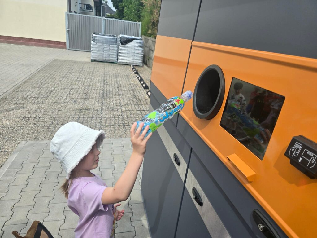 Dziecko stoi przed butelkomatem i wrzuca butelkę do otworu.