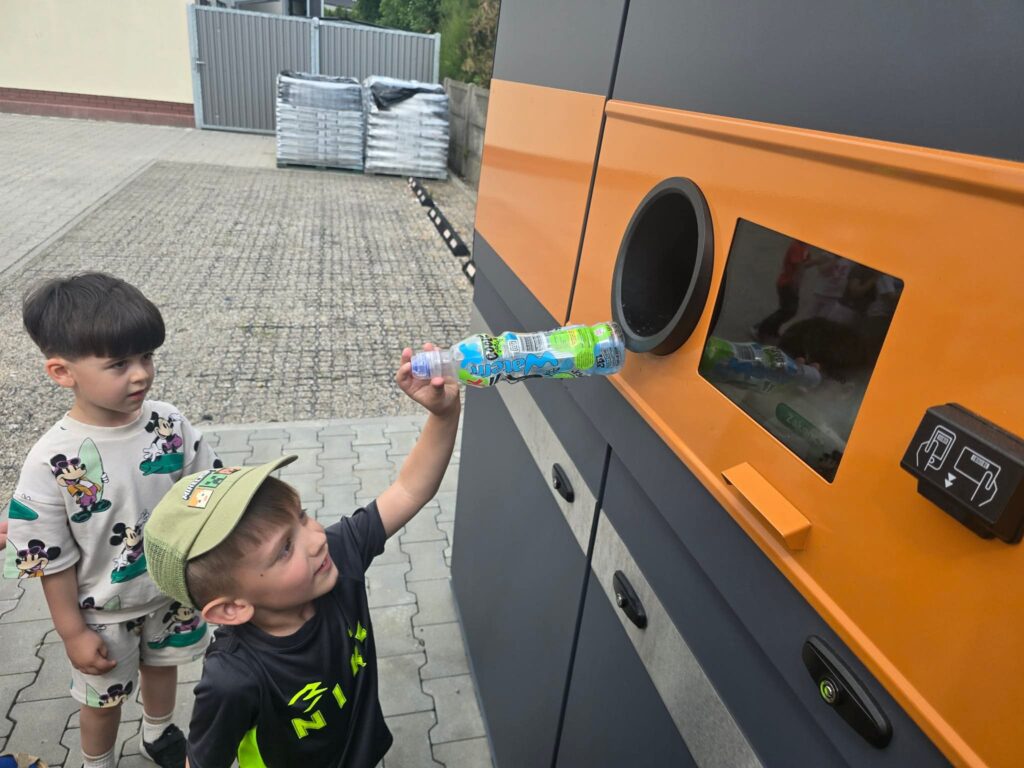 Dziecko stoi przed butelkomatem i wrzuca butelkę do otworu.