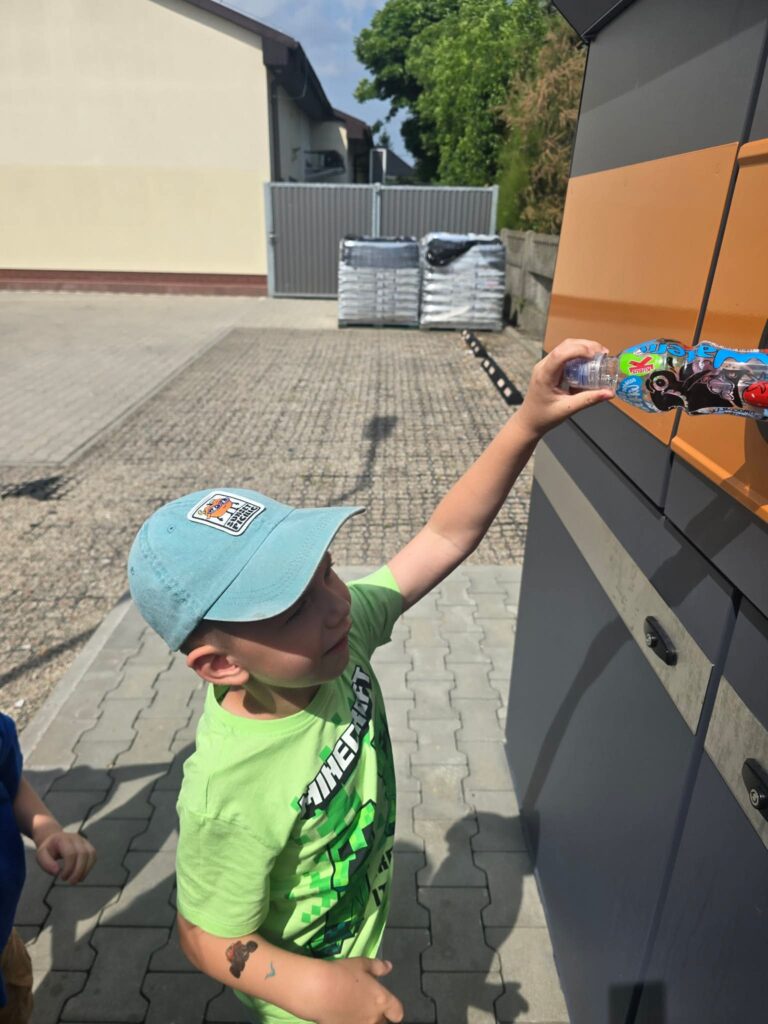 Dziecko stoi przed butelkomatem i wrzuca butelkę do otworu.
