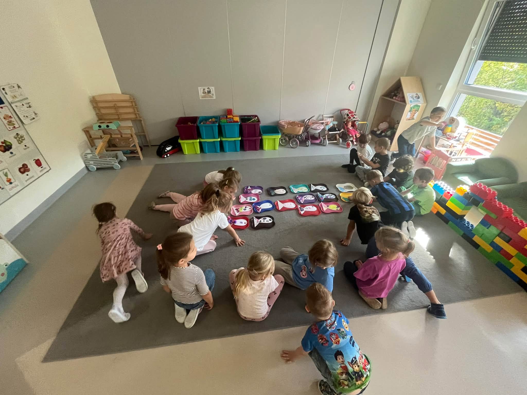 Dzieci siedzą na dywanie, obok leżą ich prace plastyczne - ryby